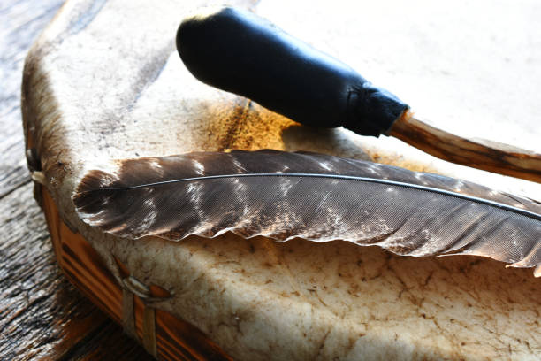 A close up image of a hand made leather meditation drum with sacred feather and drum stick.